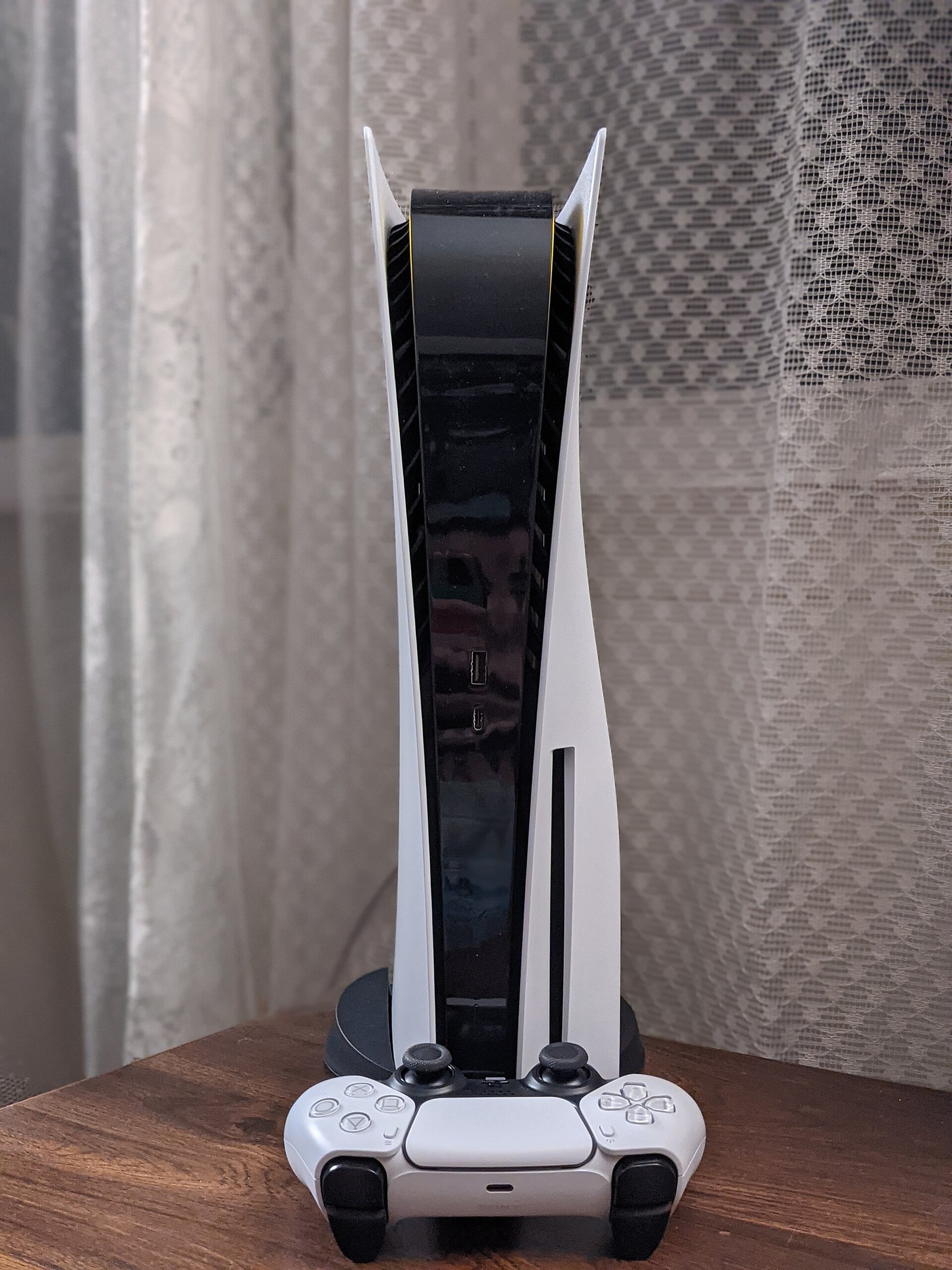Une PlayStation 5 blanche posée à la verticale, avec sa manette DualSense devant elle